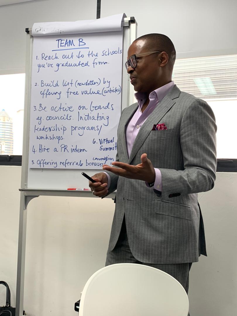 David McKnight in a grey pinstripe suit teaching beside a whiteboard of notes