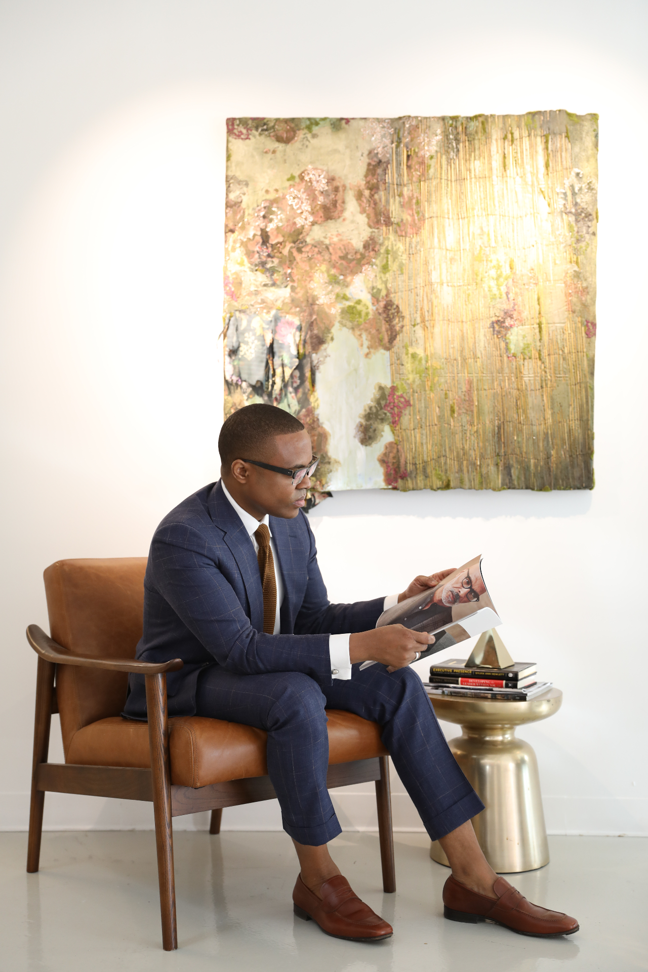 David McKnight reading in a leather armchair beneath a large artwork