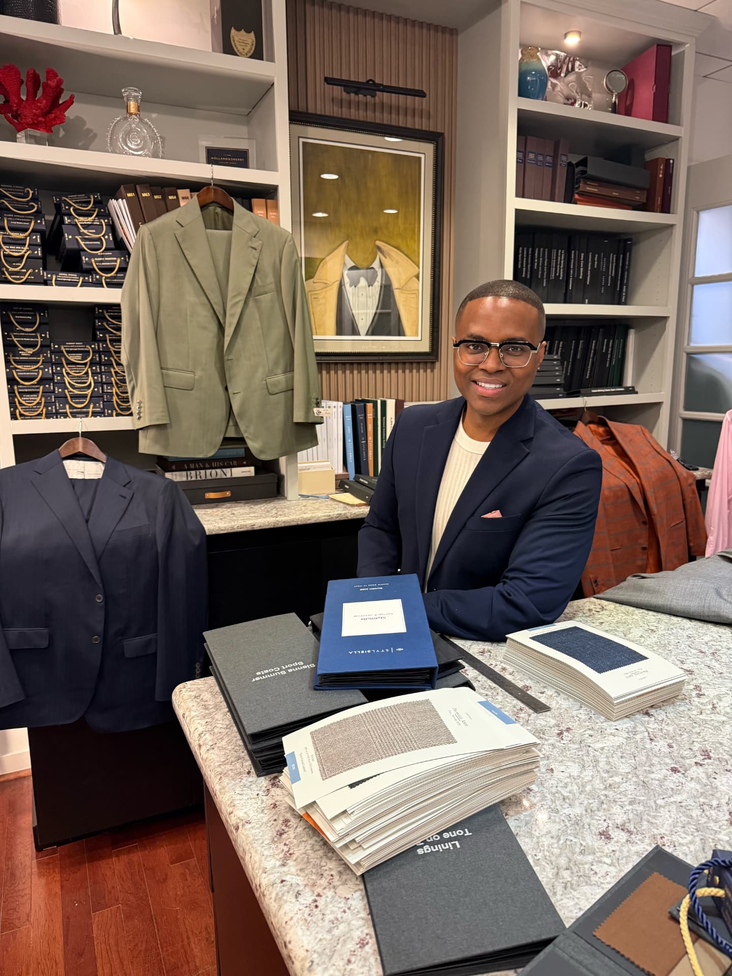 David McKnight smiling at the tailor's counter, wearing a navy blazer over a cream knit top