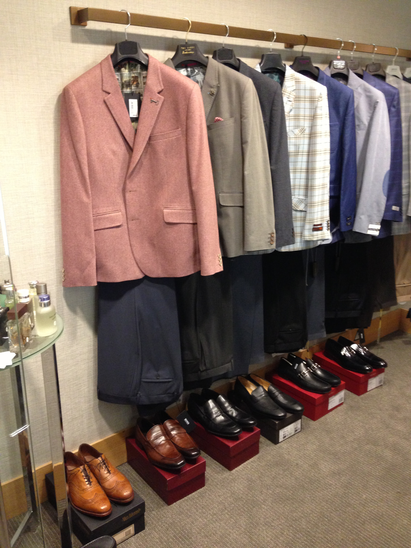 A rack of blazers above rows of leather dress shoes on their boxes