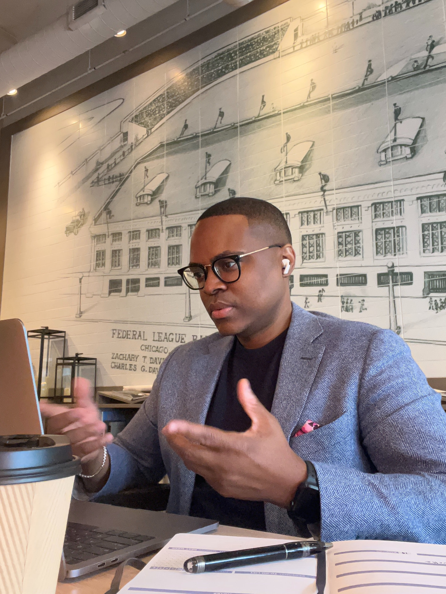 David McKnight gesturing with both hands at a laptop during a video call in a cafe