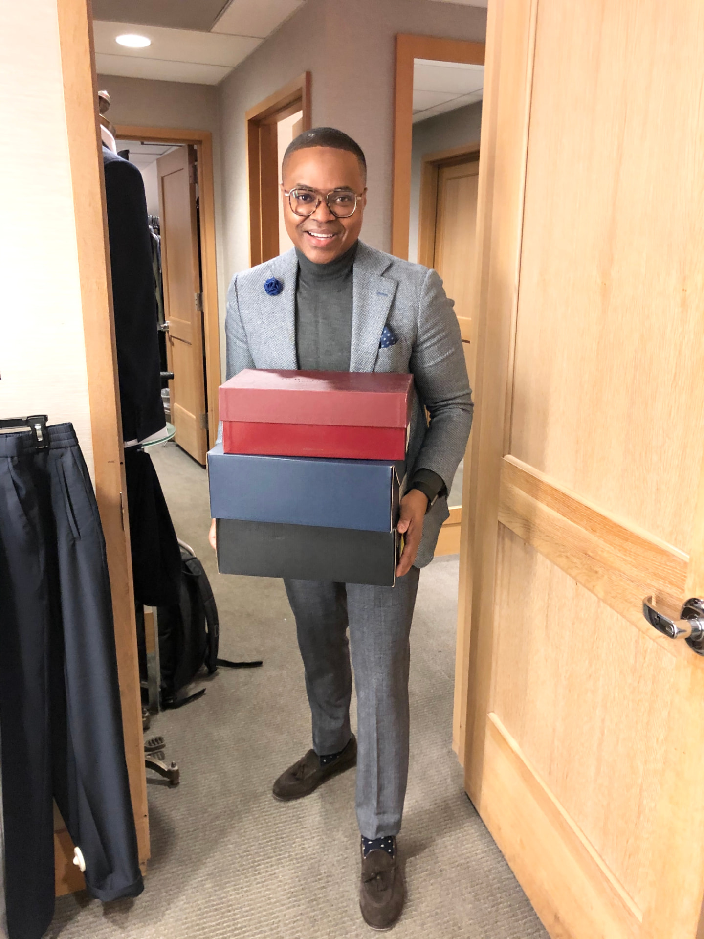 David McKnight smiling in a light grey suit while carrying a stack of three shoe boxes
