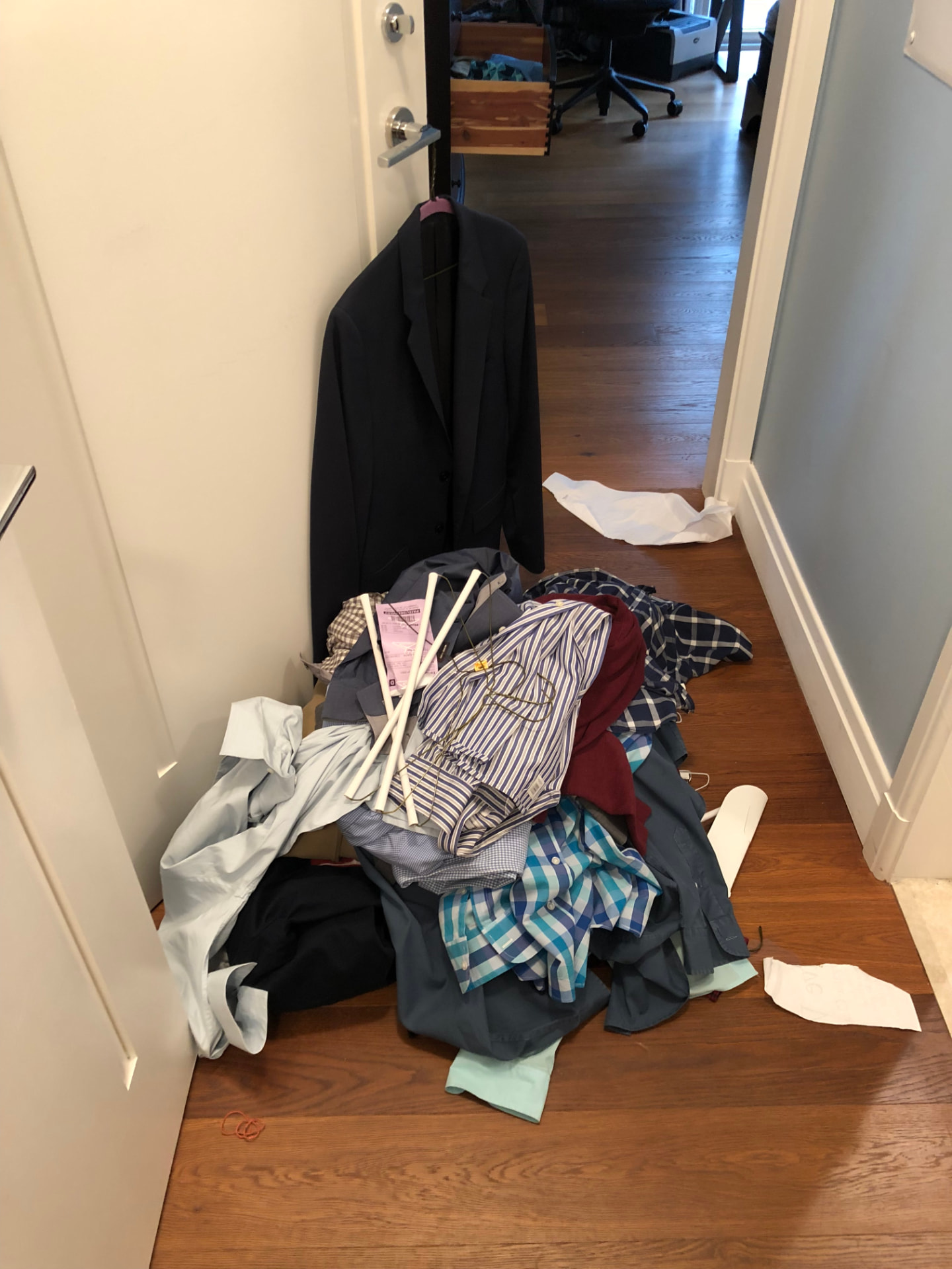 Clothes and hangers sorted into a pile in a hallway during a wardrobe edit, with a dark blazer hanging on the door