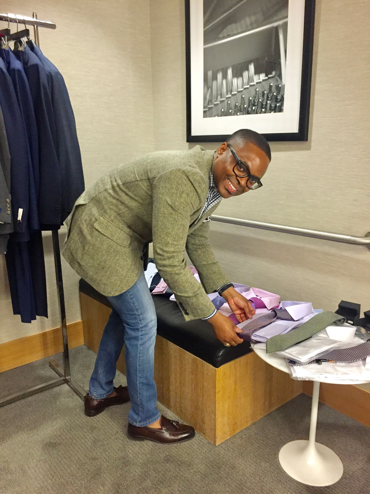 David McKnight leaning on a bench in a tweed blazer, gingham shirt and jeans